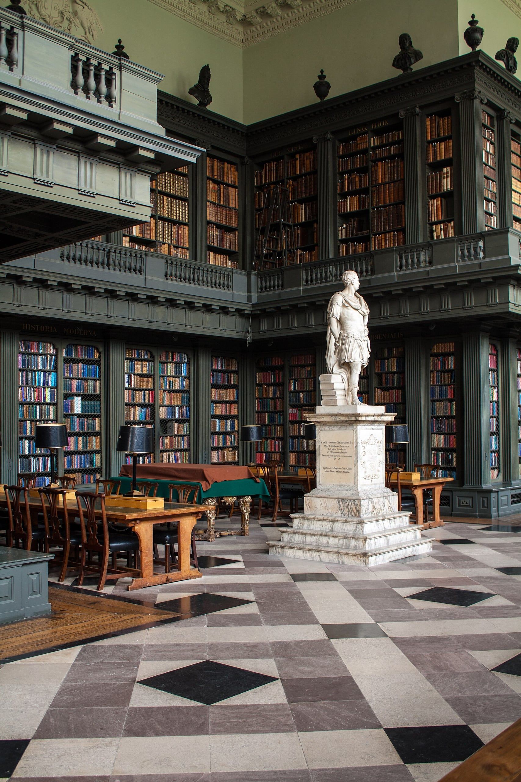 The Codrington Library at All Souls College, Oxford: tall bookcases, reading tables and a marble statue on a chequered floor.