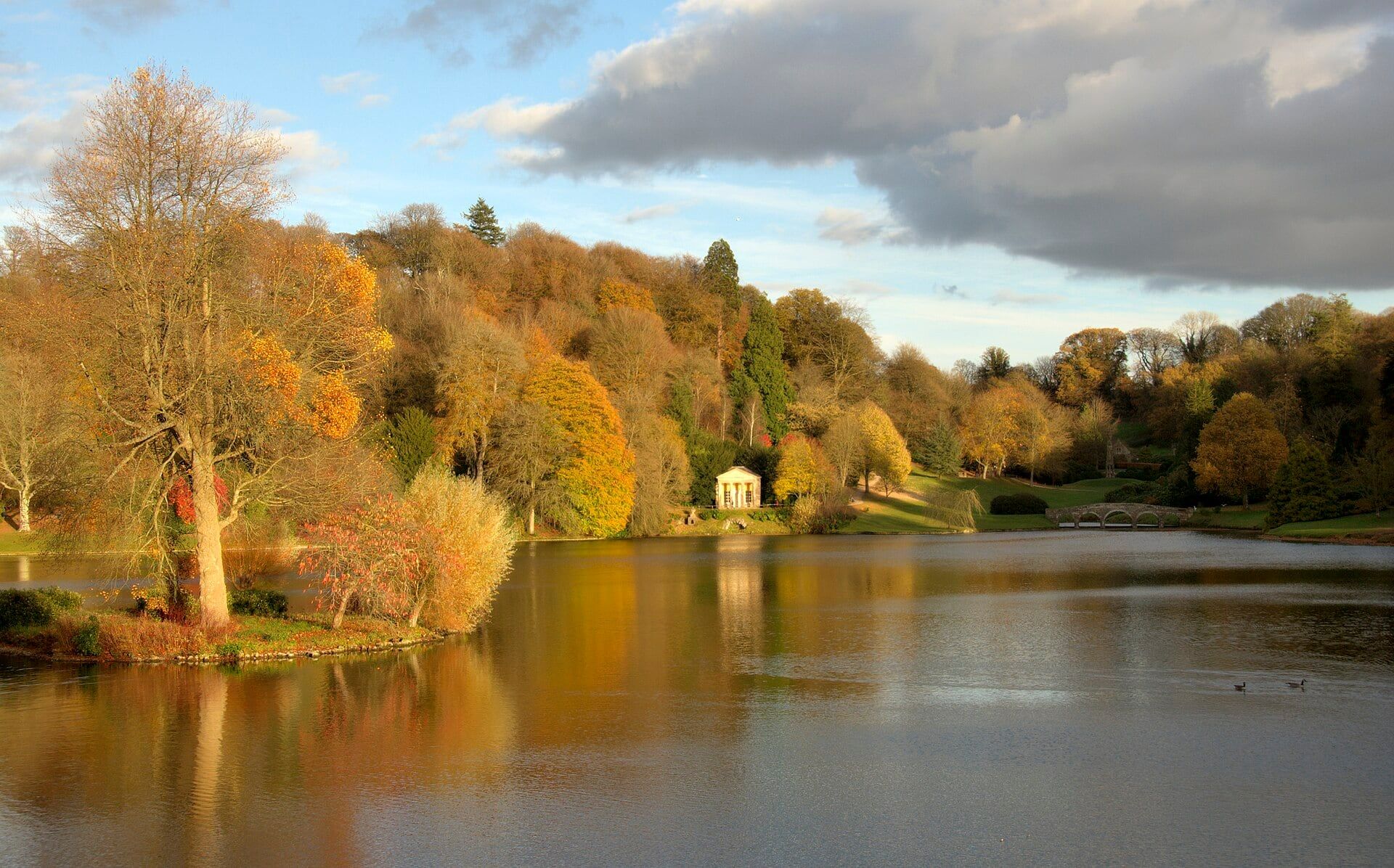 The lake at Stourhead in autumn, with golden trees and a classical temple reflected in the water.