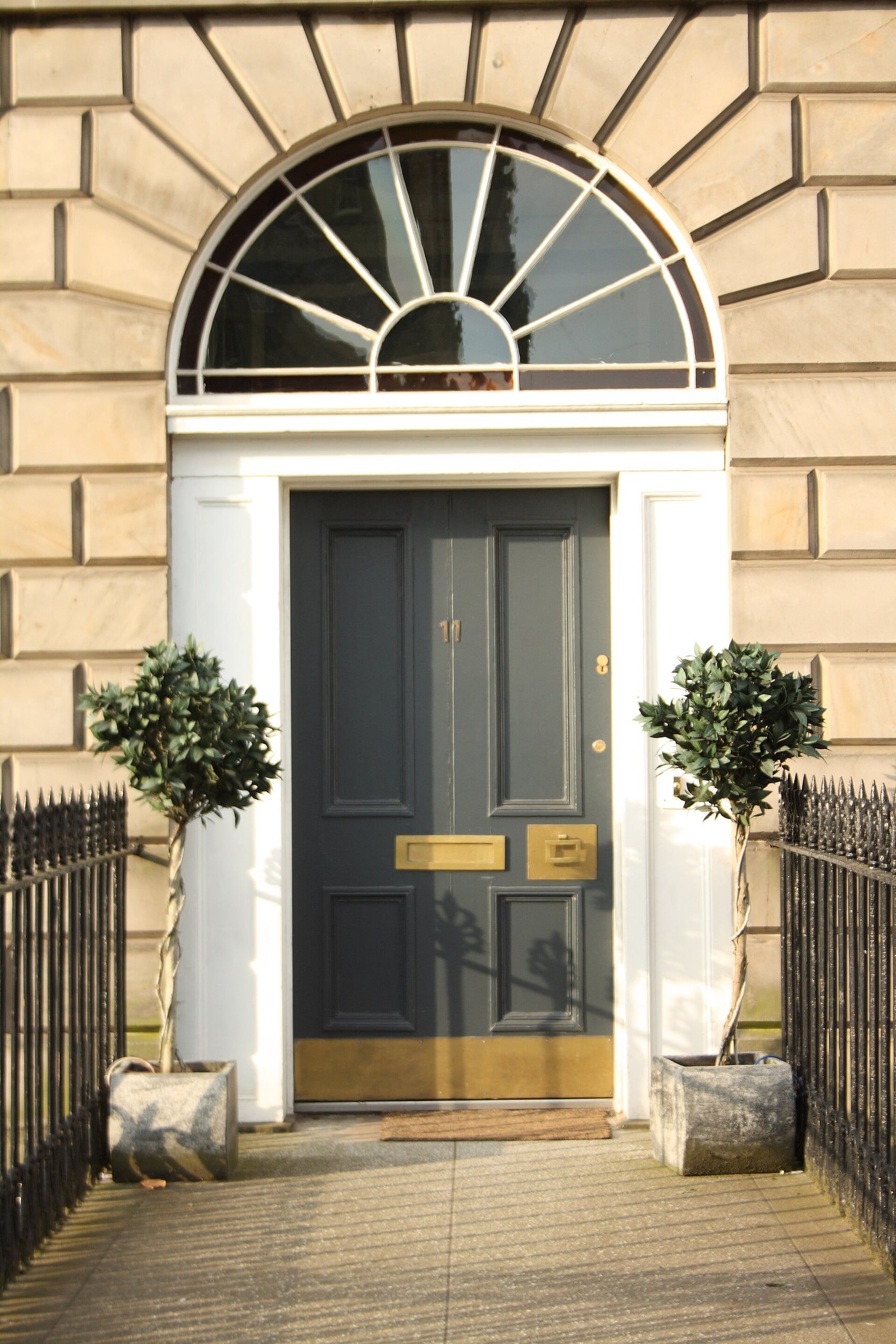 A Georgian front door in Edinburgh, painted charcoal with brass fittings, under a fanlight and between clipped bay trees.